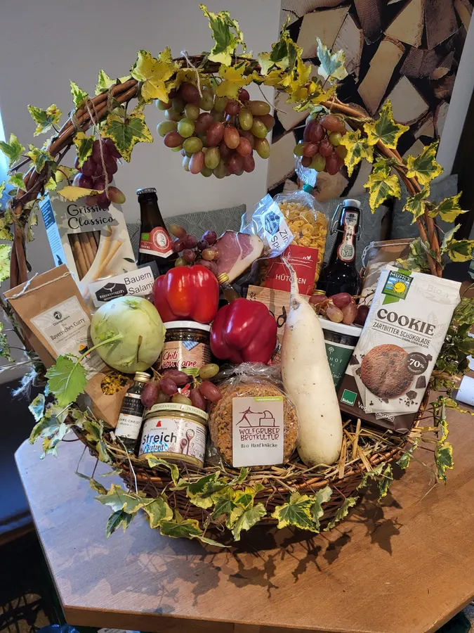 Geschenkkorb mit Trauben, Efeu, Wein, Äpfeln, Paprika und Feinkost